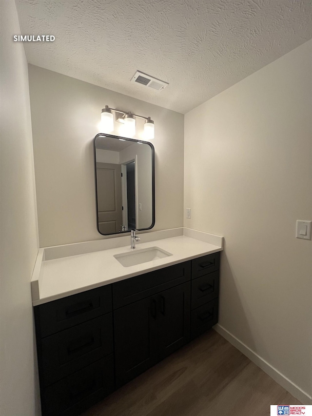 bathroom with wood finished floors, vanity, baseboards, visible vents, and a textured ceiling
