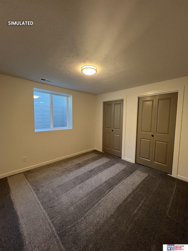unfurnished bedroom featuring multiple closets, baseboards, visible vents, dark carpet, and a textured ceiling