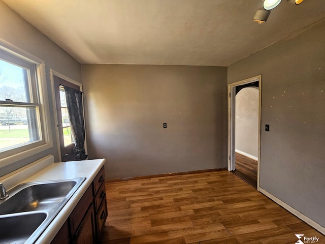 kitchen featuring baseboards, wood finished floors, light countertops, and a sink