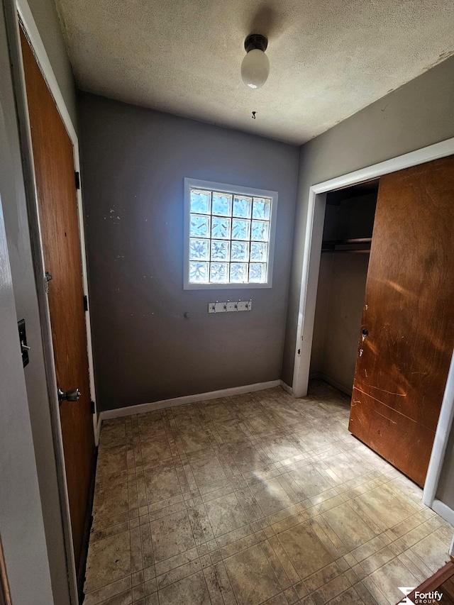unfurnished bedroom featuring a textured ceiling, a closet, tile patterned floors, and baseboards
