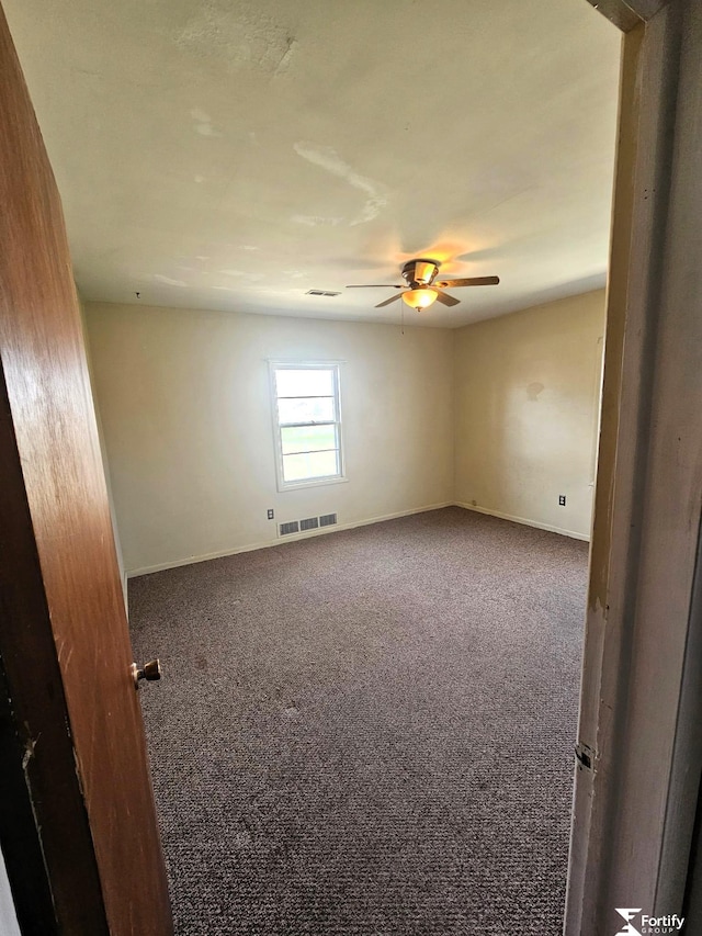 carpeted empty room with baseboards, visible vents, and a ceiling fan