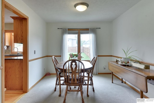 dining space with baseboards and light colored carpet
