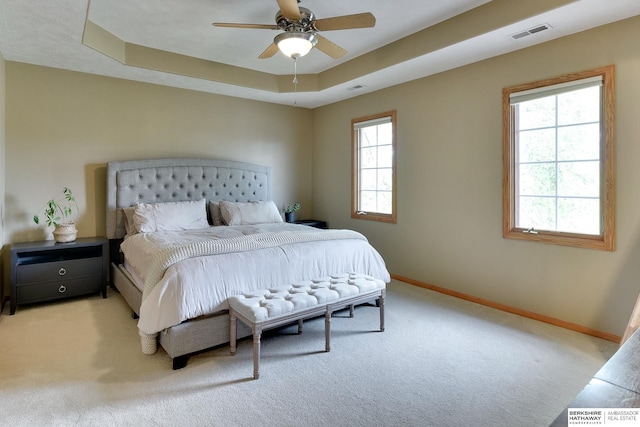 bedroom with baseboards, light carpet, a tray ceiling, and visible vents