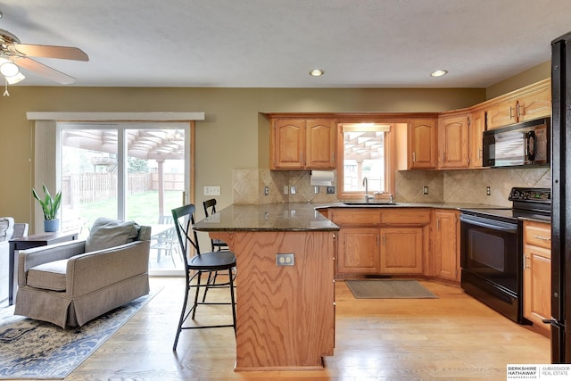 kitchen with a peninsula, a kitchen breakfast bar, a sink, light wood-style flooring, and black appliances