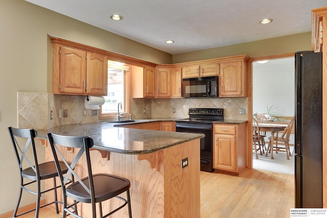 kitchen with a peninsula, a kitchen breakfast bar, a sink, light wood finished floors, and black appliances