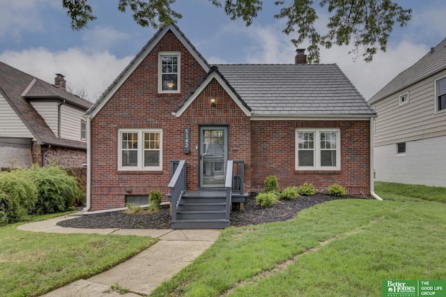 tudor house with a chimney, brick siding, and a front yard