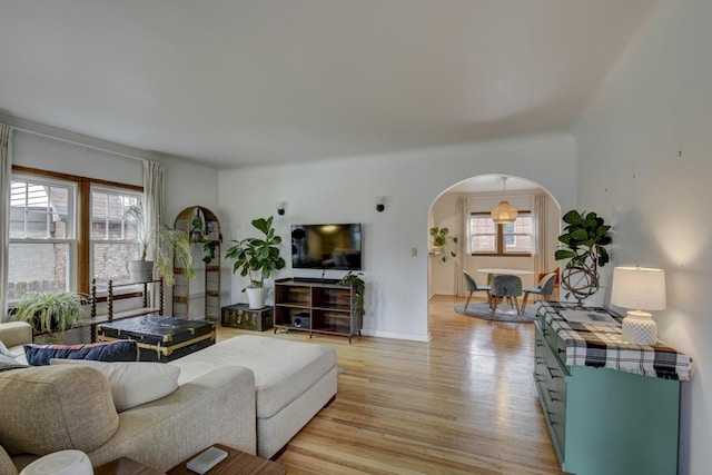 living area featuring light wood-style floors, baseboards, and arched walkways