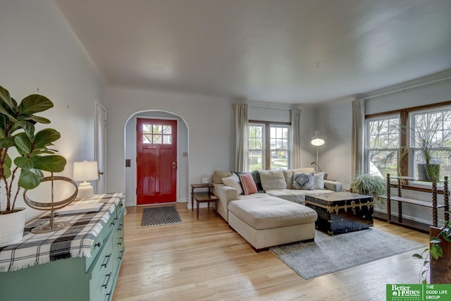 living room featuring a wealth of natural light, baseboards, light wood finished floors, and arched walkways
