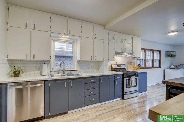 kitchen with a sink, appliances with stainless steel finishes, light wood-style floors, light countertops, and under cabinet range hood
