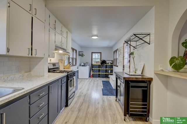 kitchen featuring white cabinetry, tasteful backsplash, light wood-style flooring, gas range, and under cabinet range hood