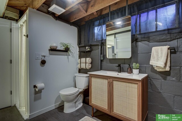 bathroom with toilet, vanity, concrete block wall, and wood finished floors