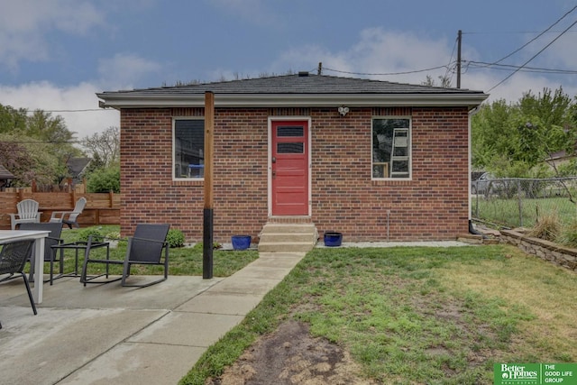 view of front of house with entry steps, a patio area, fence, brick siding, and a front lawn