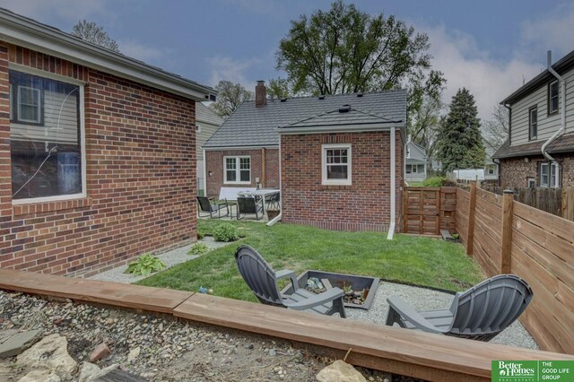 back of house featuring brick siding, a fenced backyard, a lawn, a chimney, and a fire pit