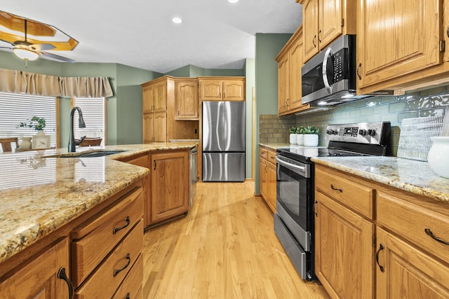kitchen with stainless steel appliances, a sink, light wood-style floors, a ceiling fan, and light stone countertops