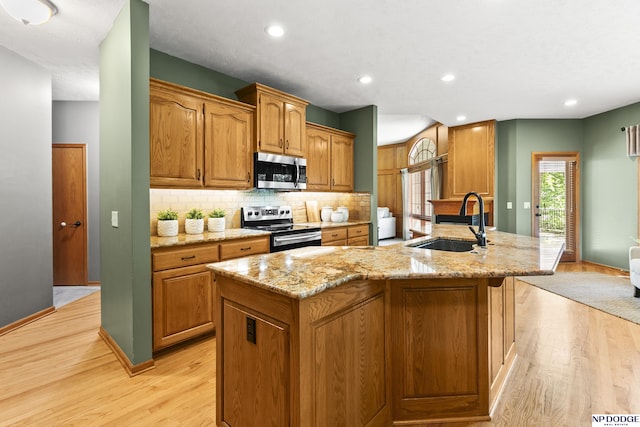 kitchen featuring appliances with stainless steel finishes, a sink, light wood-type flooring, tasteful backsplash, and light stone counters