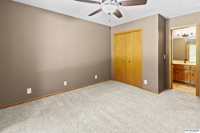 unfurnished bedroom with light colored carpet, baseboards, a closet, ceiling fan, and ensuite bathroom