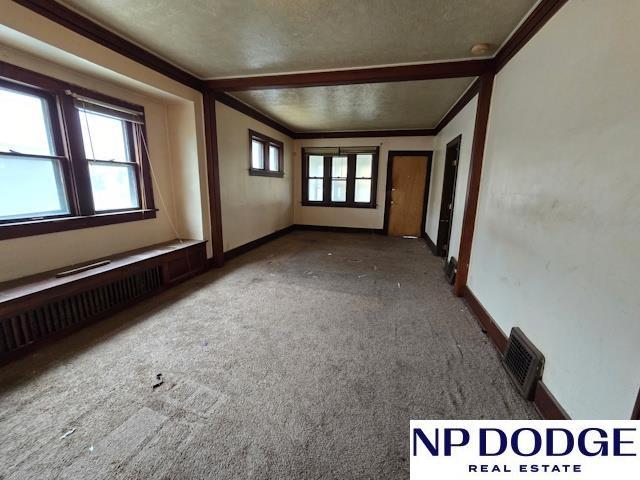 carpeted empty room featuring a textured ceiling, visible vents, crown molding, and baseboards