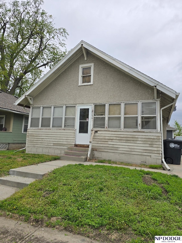 bungalow-style home featuring a front yard, entry steps, and stucco siding