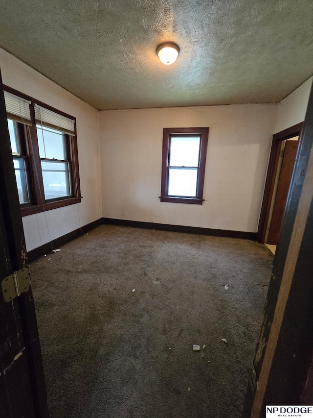 spare room with a textured ceiling, carpet, and baseboards