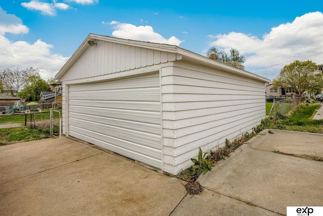 detached garage featuring concrete driveway and fence