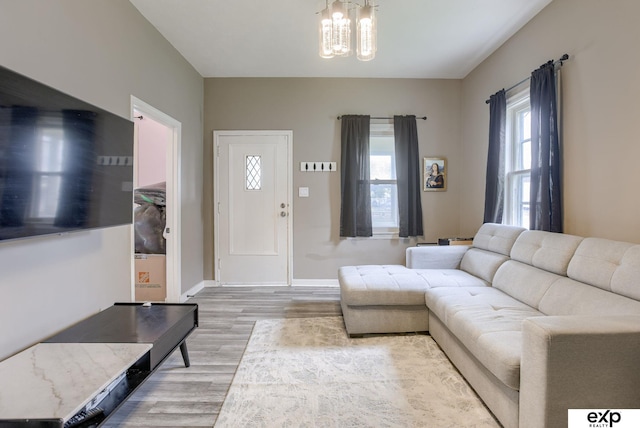 living area with an inviting chandelier, a wealth of natural light, light wood-type flooring, and baseboards