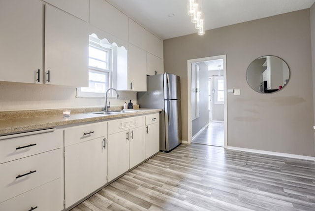 kitchen with white cabinetry, a sink, freestanding refrigerator, and light countertops