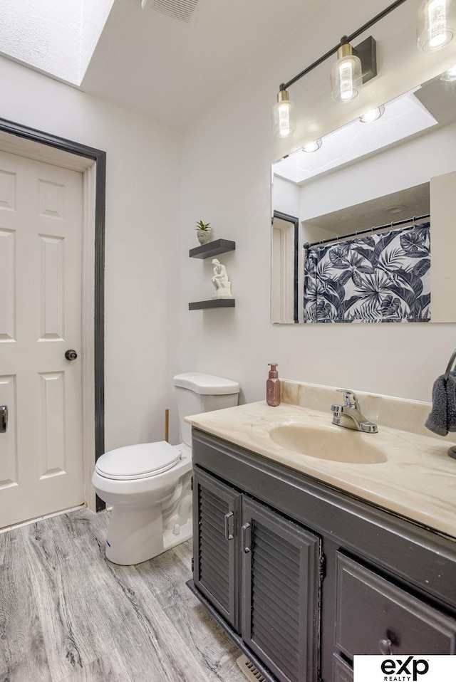 bathroom featuring visible vents, toilet, wood finished floors, vanity, and a skylight