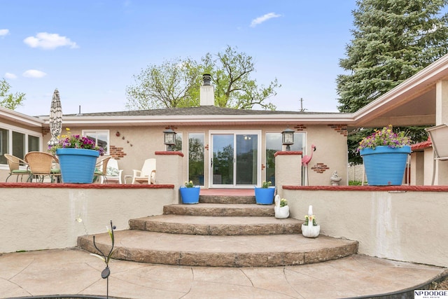 back of property featuring a chimney, entry steps, and stucco siding