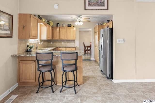 kitchen featuring a peninsula, a sink, stainless steel fridge with ice dispenser, baseboards, and light stone counters