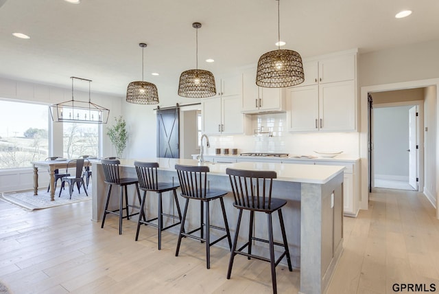 kitchen featuring recessed lighting, an island with sink, a barn door, light countertops, and backsplash