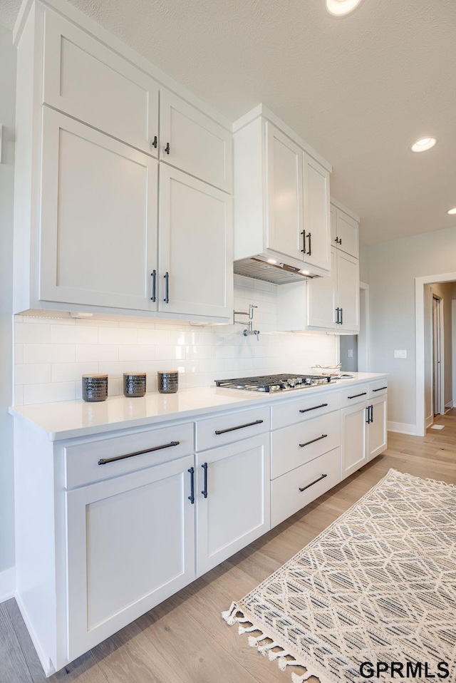 kitchen with baseboards, white cabinets, stainless steel gas cooktop, and light wood finished floors