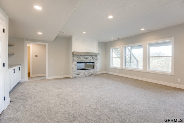unfurnished living room with recessed lighting, visible vents, a stone fireplace, baseboards, and light colored carpet