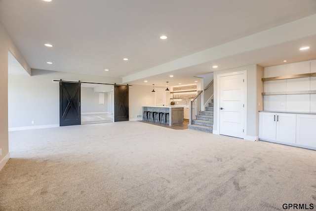 unfurnished living room featuring light colored carpet, a barn door, baseboards, recessed lighting, and stairs