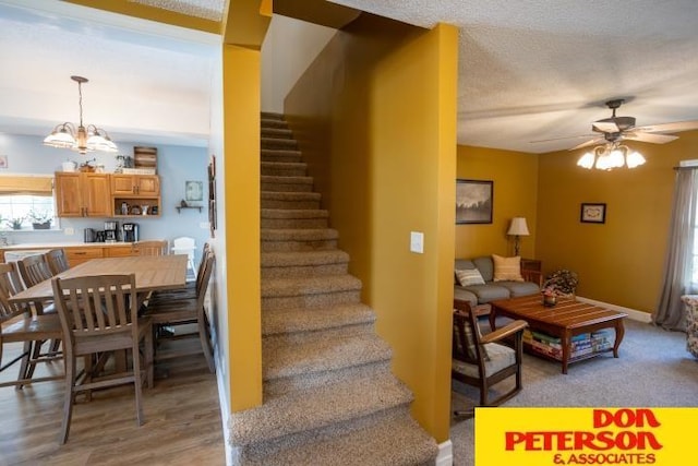 stairway featuring a textured ceiling and ceiling fan with notable chandelier