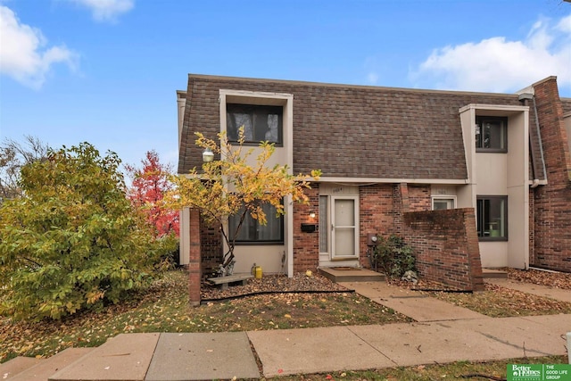 view of front of home featuring mansard roof, a shingled roof, and brick siding
