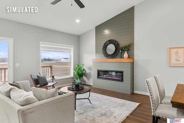 living area featuring a healthy amount of sunlight, a large fireplace, ceiling fan, and wood finished floors