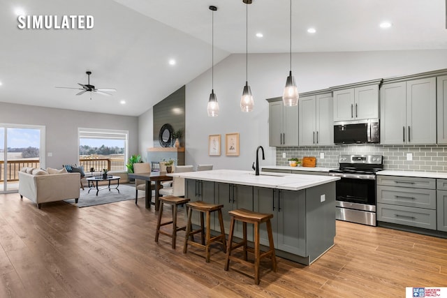 kitchen featuring a sink, high vaulted ceiling, gray cabinets, stainless steel appliances, and a center island with sink