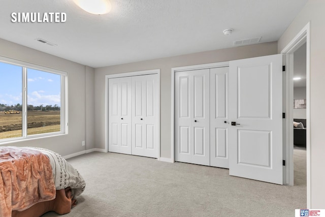 bedroom featuring multiple closets, baseboards, light carpet, and visible vents
