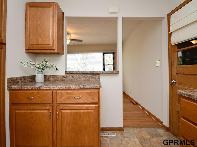 kitchen with baseboards, a ceiling fan, brown cabinets, and visible vents