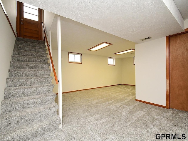 below grade area featuring a textured ceiling, visible vents, baseboards, carpet flooring, and stairs