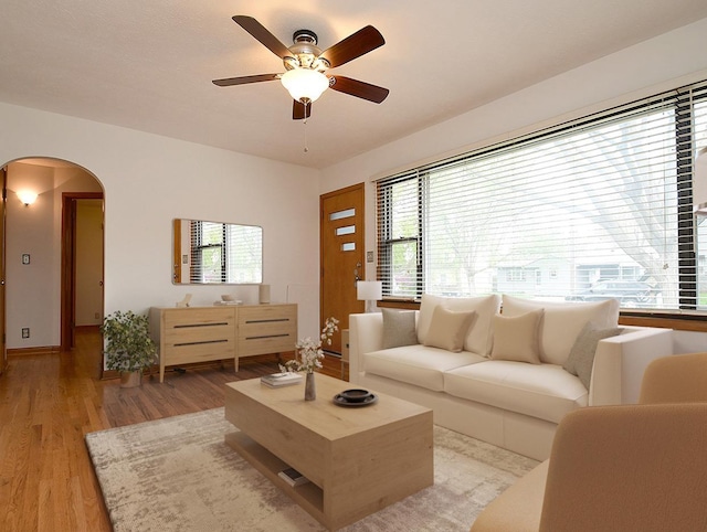 living room with light wood-type flooring, arched walkways, plenty of natural light, and ceiling fan