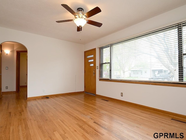 unfurnished room with a ceiling fan, visible vents, arched walkways, baseboards, and light wood finished floors