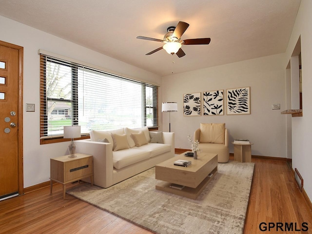 living area with baseboards, ceiling fan, and wood finished floors
