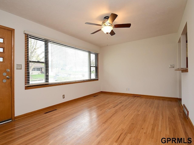 unfurnished room featuring baseboards, light wood finished floors, ceiling fan, and a healthy amount of sunlight