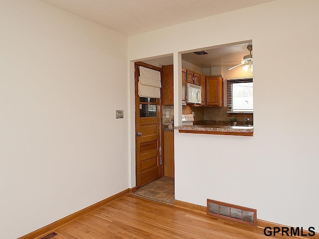kitchen featuring brown cabinetry, visible vents, baseboards, white microwave, and light wood-style floors