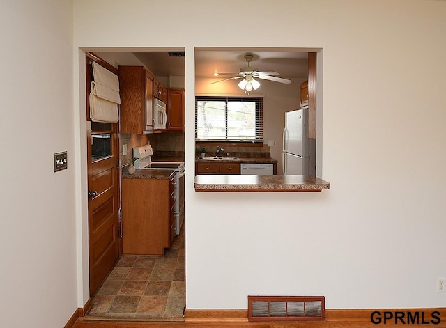 kitchen featuring stone finish floor, a ceiling fan, visible vents, dark countertops, and white appliances