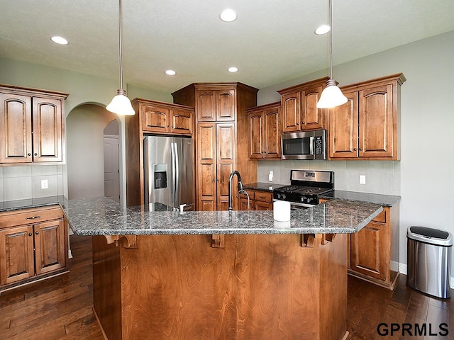 kitchen featuring stainless steel appliances, arched walkways, dark wood-type flooring, brown cabinets, and recessed lighting