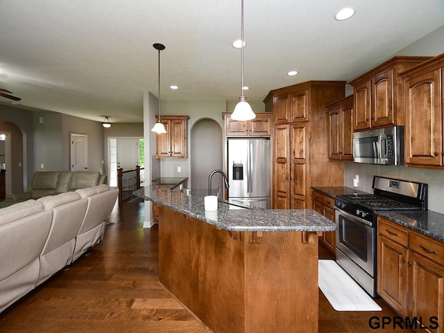kitchen featuring stainless steel appliances, arched walkways, open floor plan, a sink, and brown cabinets