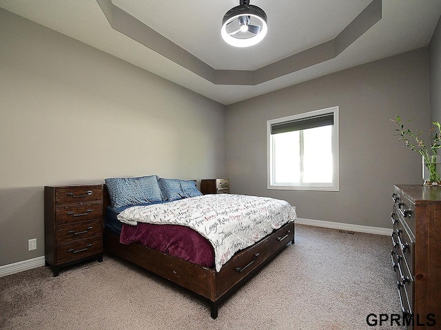 bedroom featuring light carpet, baseboards, and a raised ceiling