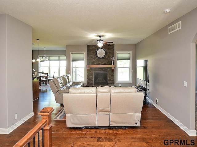 living room featuring a ceiling fan, dark wood-type flooring, baseboards, a large fireplace, and plenty of natural light